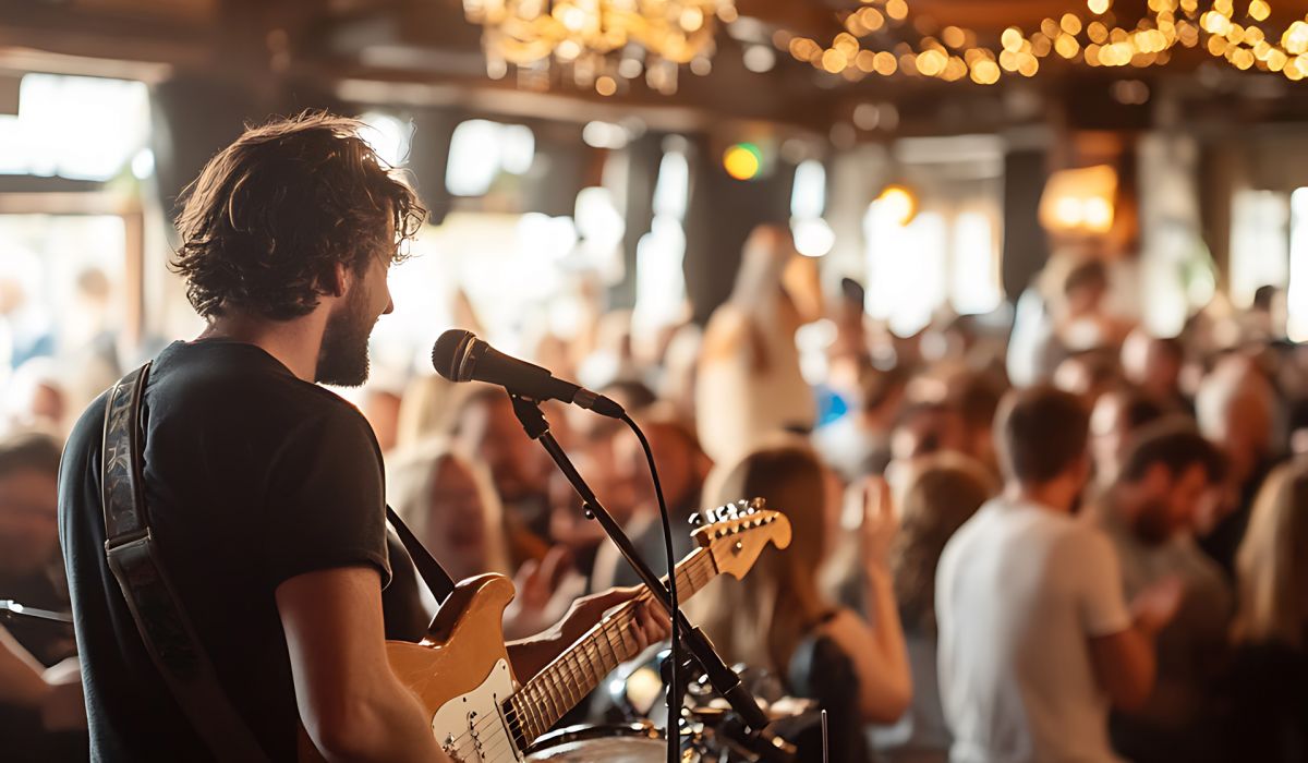 Magnolia A musician plays electric guitar on stage in a lively, crowded bar with warm lighting and audience applause.
