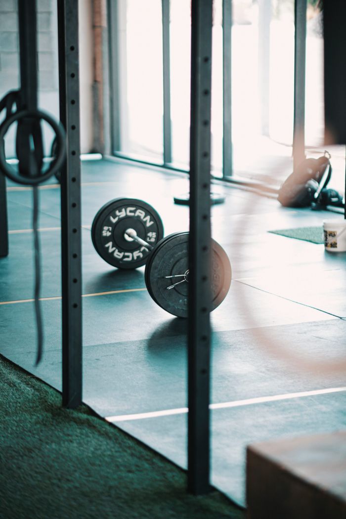 Magnolia A barbell with weight plates rests on a gym floor, surrounded by racks and gym equipment in natural light.