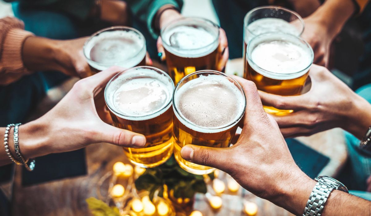 Magnolia Six people holding glasses of beer, toasting together over a table decorated with candles and greenery.